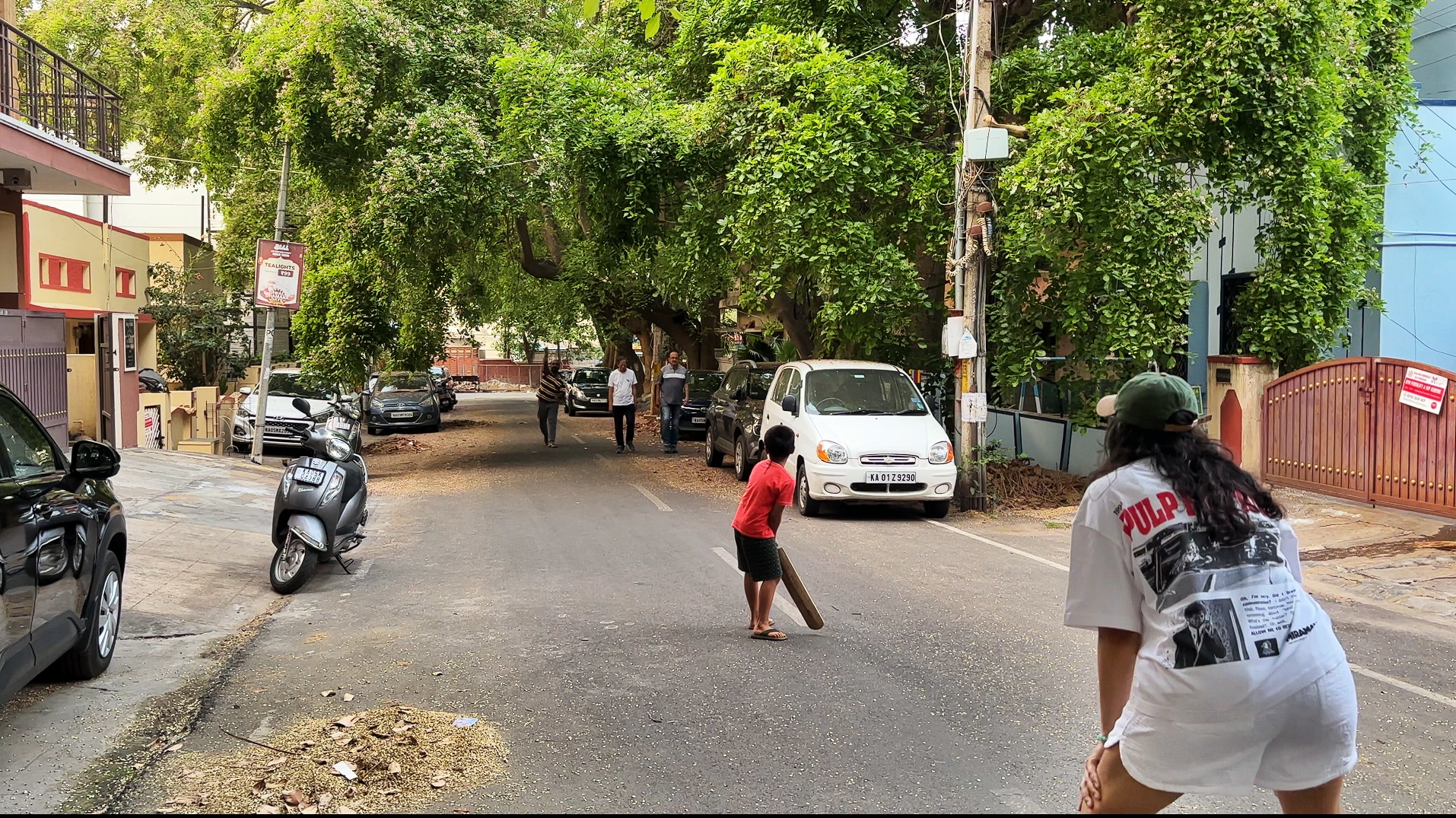 A tree-lined street in the evening, a kid batting, me crouched behind the stumps keeping wickets